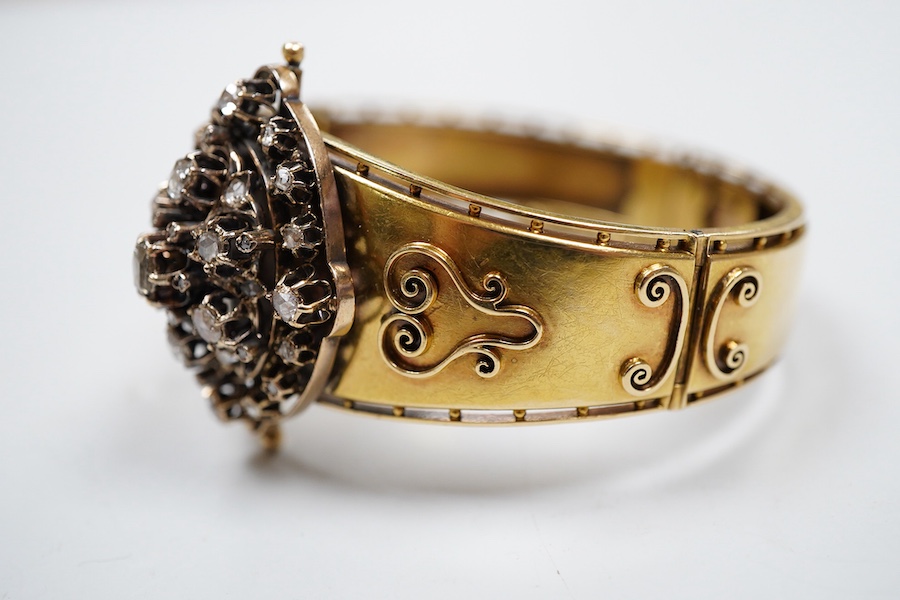 A Victorian gold and diamond bracelet, the hinged cuff decorated with wire scrollwork, centring on an oval motif set with rose-cut diamonds, inner circumference approximately 17cm, width at front 3.8cm, gross weight appr